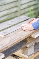 Woman marking the planks of wood at the same width as the pallet