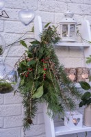 Tied bunch of evergreen foliage - conifers, ilex and Larix decidua cones attached to white ladder decorated with tealights