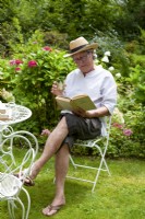Man sitting on chair on lawn reading a book
