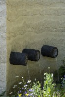 Clay rendered wall in garden with water spout pipes