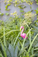 Small flamingo ornament among various plants in a border