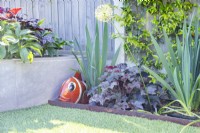 Heuchera 'Ginger Peach' planted in border next to rustic metal fish ornament