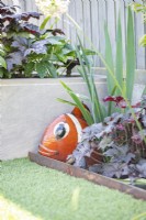 Rustic metal fish ornament next to Heuchera 'Ginger Peach'