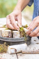 Woman placing moss inbetween the pieces of birch