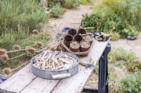 Half completed hanging bee hotel, dried Dipsacus - Teasel stems, secateurs and gloves laid out on a wooden surface