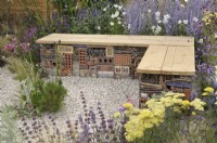 Bug or insect hotel packed inside a gabion basket with wooden bench top - Turfed Out Garden, RHS Hampton Court Palace Garden Festival 2022.  July.  Designer: Hamzah-Adam Desai  
