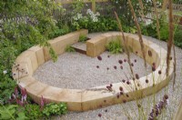 Sunken gravel garden with circular timber block seating in The Wooden Spoon Garden, RHS Hampton Court Palace Garden Festival 2022.  Designers:  Toni Bowater and Lucy Welsh