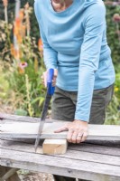 Woman sawing the wooden planks to the correct lengths
