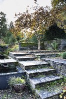 Steps leading up to terraces with water feature in a country garden in November