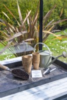 Fibre pots, watering can, pen, labels, compost and sunflower seeds laid out on a table
