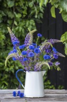 Centurea cyanus - Cornflowers arranged with blue lupins in white enamel jug on table
