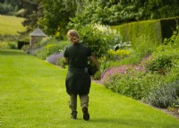 A gardener carrying a large plant in a pot along the lawn between the double borders at Newby Hall.