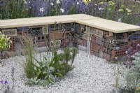 Gabion bench with insect hotels bordered by pink and purple themed perennial planting in Turfed Out at RHS Hampton Court Palace Garden Festival 2022