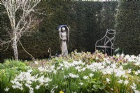 Angel by John Aulman in yew wood with border full of hellebores and daffodils in the foreground