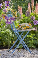 Straw hat with wreath of summer flowers on the chair in front of the pink purple border with Allium, Iris and Lupinus.