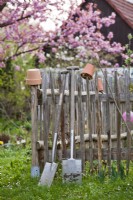 Garden tools leaning on wooden fence.