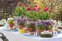Table set for Easter containing tulips in birch bark containers, violas and coloured eggs.