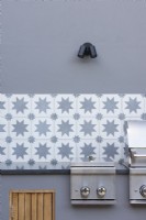 Detail of outdoor kichen with grey walls, decorative wall tiles and bbq. 
