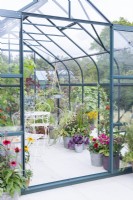 White table and chairs inside greenhouse full of various mixed planting containers
