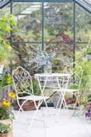 White table and chairs inside greenhouse decorated with various plants and containers