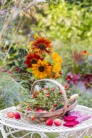 Arrangement of sunflowers next to a trug containing rosehips and crab apples on a white metal table