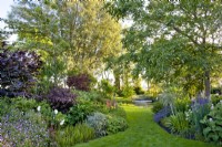 Country garden in summer with mixed perennial borders and a grass path to the pond.