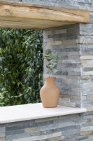 Terracotta urn set on coping in a stone clad wall - A Peaceful Escape, RHS Malvern Spring Festival 2022