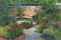 In a small private courtyard, rusted steel planters and borders  are filled with the Japanese pagoda tree and gold birch tree; Helenium 'Moerheim Beauty'; Salvia nemorosa 'Caradonna' and ornamental grasses.