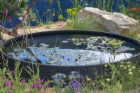 A circular raised pool is set into a gravel garden planted with colourful perennials amongst boulders.