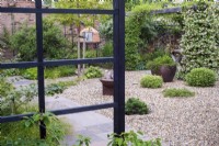 View across small Oriental inspired green garden with evergreen shrubs growing in the gravel and wooden arbor and cooking oven