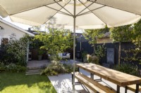 Seating area with parasol and wooden table with bench in small suburban garden