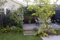 Garden patio in small suburban garden featuring Trachelospermum jasminoides and Amelanchier 'Robin Hill' 
in borders