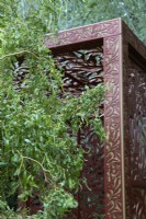 Morris  and  Co. Garden. Designer: Ruth Willmott. RHS Chelsea Flower Show 2022. Gold Medal. Detail of pavilion crafted from metal screens made from laser cut metal with 'Willow Boughs' William Morris design. With Salix Matsundana 'Tortuosa' - Dragon's claw willow.