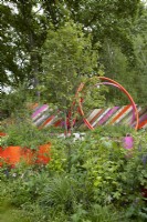 The St. Mungo's Putting Down Roots Garden. Designers: Cityscapes -Darryl Moore and Adolfo Harrison- RHS Chelsea Flower Show 2022. Silver Medal. A design for a miniature urban park using recycled materials. Bright painted planters and fencing contrast naturalistic soft planting. Summer. May.