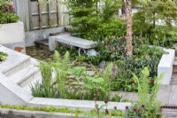 Modern garden design near house, paved area with concrete raised beds and seating. Summer July
