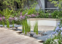 Caption: Modern garden design, decked surface near water with curved bench. Summer July