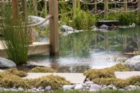Natural swimming pool with plants, pebbles and wooden deck - BBC Gardeners' World Live, Birmingham 2022 - The Living Landscape - A Nostalgic Experience garden - designer The Garden Design Company with Michael Wheat Group