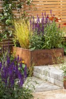 Rusted steel planters filled with perennials with benches, wooden fence, steps, and clay paver and gravel paths - RHS Hampton Court Palace Garden Festival, London, July 2022 - 'Lunch Break Garden', Best in Show Get Started Gardens - Designer Inspired Earth Design