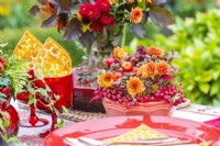 Bowl containing chrysanthemums, crab-apples, succulents and berries next to red tableware set