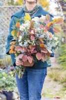 Woman holding an arrangement of Cotinus 'Grace', Eucalyptus 'Silver Dollar', Eryngium 'Picos Blue', Anemone 'Ruffled Swan' and Astrantia 'Snow Star'