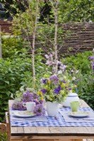 Table set with vase of spring flower bouquet containing allium, iris, wild flower perennials and grasses.