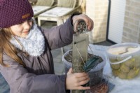 Girl filling bird feeder with sunflower seeds on snowy day in winter