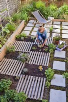 Woman creating drought tolerant flowerbed on the roof of garage. The flower bed is separated by slats, which are decorative and at the same time serve as a path. Planting Sedum spathulifolium - Stonecrop.