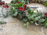 Fresh foliage and berries being wired into wreath covered with moss