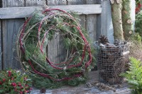 Wreath made of pine branches, clematis tendrils and woollen string, basket with cones