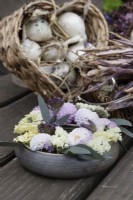 A hand made pottery posy ring sat on a wooden table top with dried hydrangea flower heads, dried purple french beans and onions. The posy ring is filled with dahlias, zinnias, eucalyptus, verbena and statice. Foam free arrangement. Autumn.