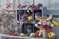 Colorful autumn decoration with bouquet of chrysanthemums, roses, snowberries, Chinese lanterns, apples, ornamental apples, quinces, balls of heather in clay pots