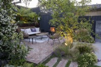 Patio area in suburban garden at sunset with lighting, seating and log burner