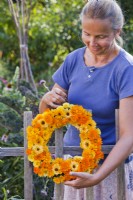 Woman hanging wreath of pot marigolds on a fence.