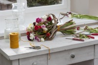 Tied spring bouquet of ranunculus and dried stalks of Chinese silver grass lying on a work table